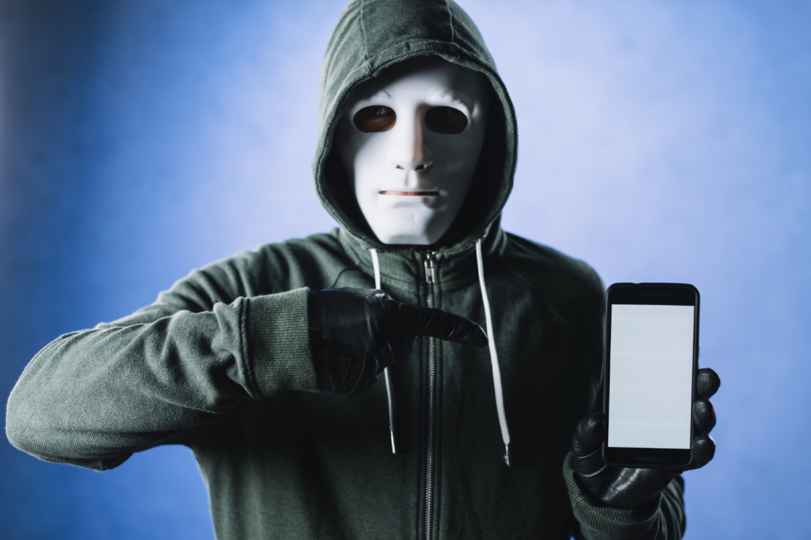 A man in a mask gestures towards his phone, holding it up as if sharing information or discussing its content.