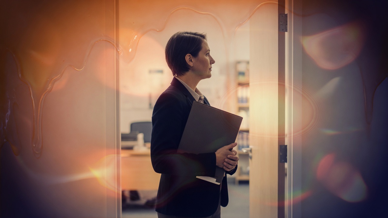 An adult with a folder standing in an office doorway under peach glass light